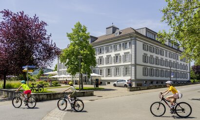 Weisses Haus Ebnet mit blauem Himmel und Radfahrern vorne im Bild